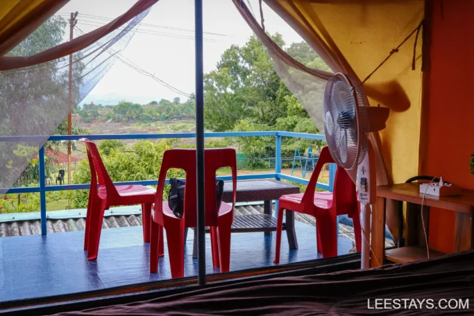 View from inside a tent with red plastic chairs on a patio overlooking lush greenery at lakeview cottages in Pawna.