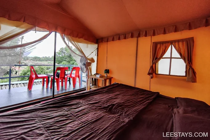 Interior of a cozy lakeview cottage in Pawna with a bed, seating area, and a view of the outdoors through a transparent door.