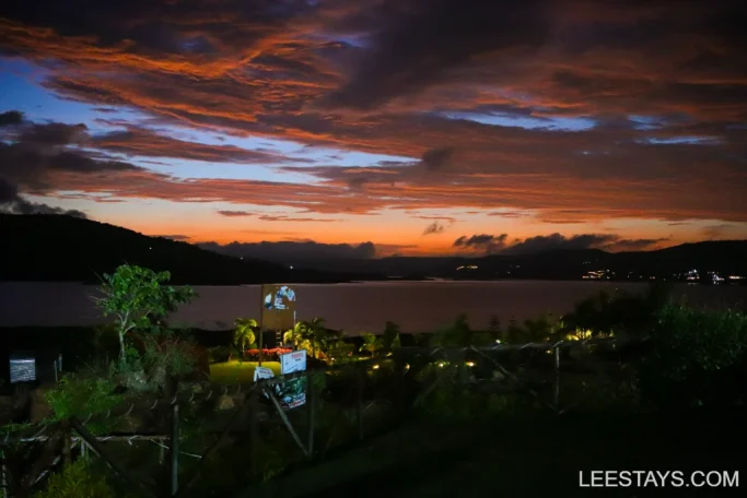 Lakeside retreat at Pawna with vibrant sunset skies reflecting on the water, surrounded by lush greenery and hills in the background.
