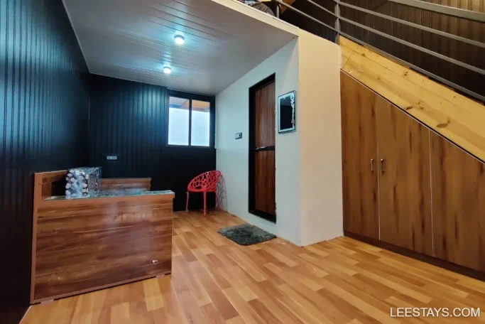 Cozy interior of a lakeside retreat in Pawna, featuring a wooden bench, red chair, and staircase in a warm, inviting setting.