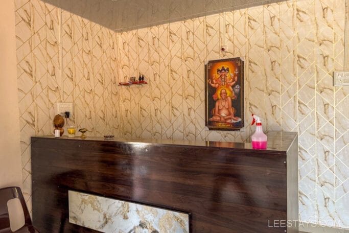 Reception area of a budget stay near Pawna Lake with a wooden desk, a religious painting on the wall, and few decorative items.