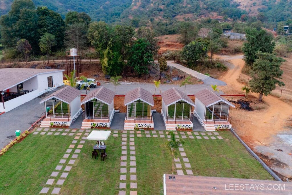 Five cozy cottages arranged in a row, ideal for a budget stay near Pawna Lake, surrounded by lush greenery and hills.