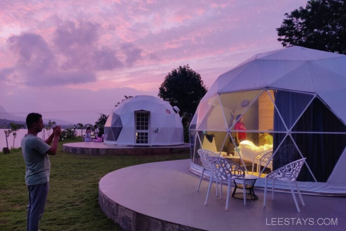 Luxurious geodesic domes at Domestory Resort during sunset, with one dome illuminated and outdoor seating visible, surrounded by a serene landscape.