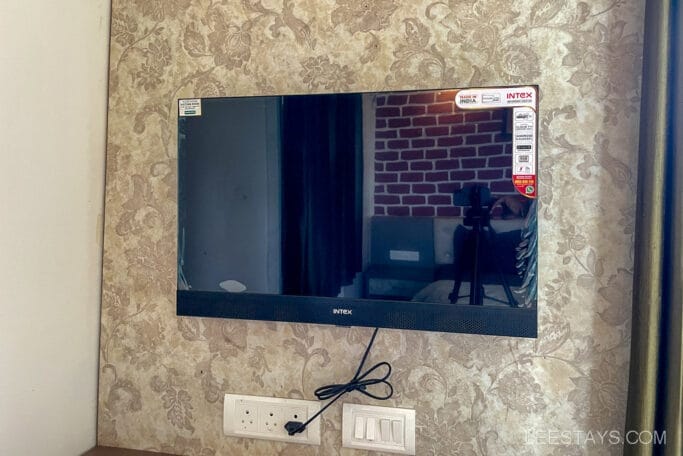 A wall-mounted Intex television in a room with floral wallpaper, possibly in a riverside cottage near Pawna Lake.