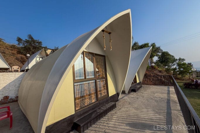 Modern glamping cottages near Pawna Lake with curved white roofs, situated on a raised platform with scenic views and outdoor seating.