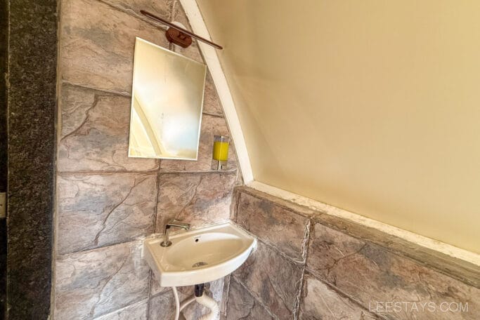 Bathroom sink and mirror in a glamping site near Pawna Lake, featuring stone tiles and a slanted wall, indicating a rustic yet modern design.