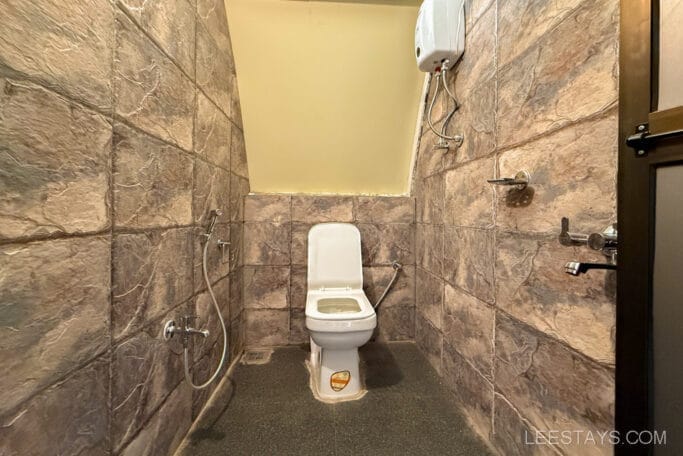A bathroom with stone-tiled walls featuring a white toilet and a handheld bidet sprayer.