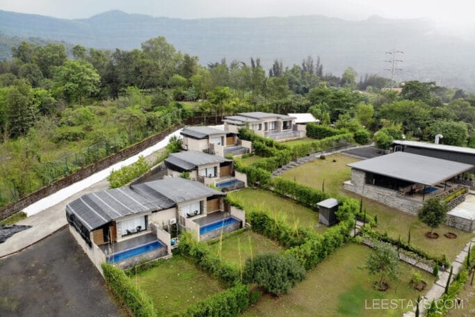 Aerial view of a resort near Pawna Lake, featuring modern cottages with individual pools surrounded by lush greenery and hills in the background.