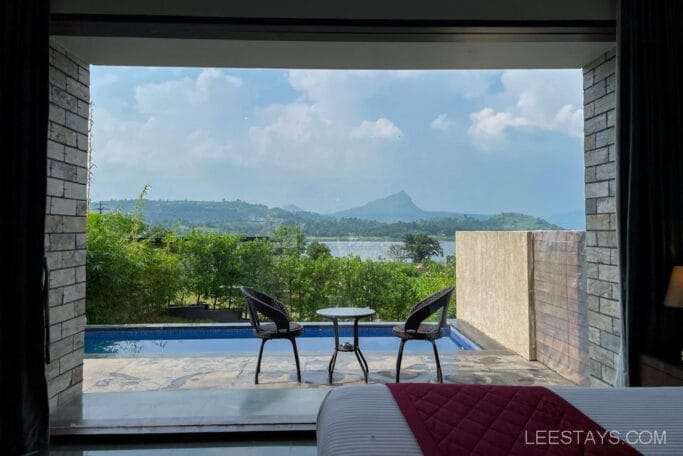 View from a resort overlooking Pawna Lake, featuring a patio with two chairs and a table beside a small pool, with hills visible in the background.