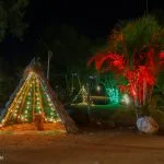 A decorated teepee with string lights at a campsite near Pawna Lake, surrounded by illuminated trees and plants at night.