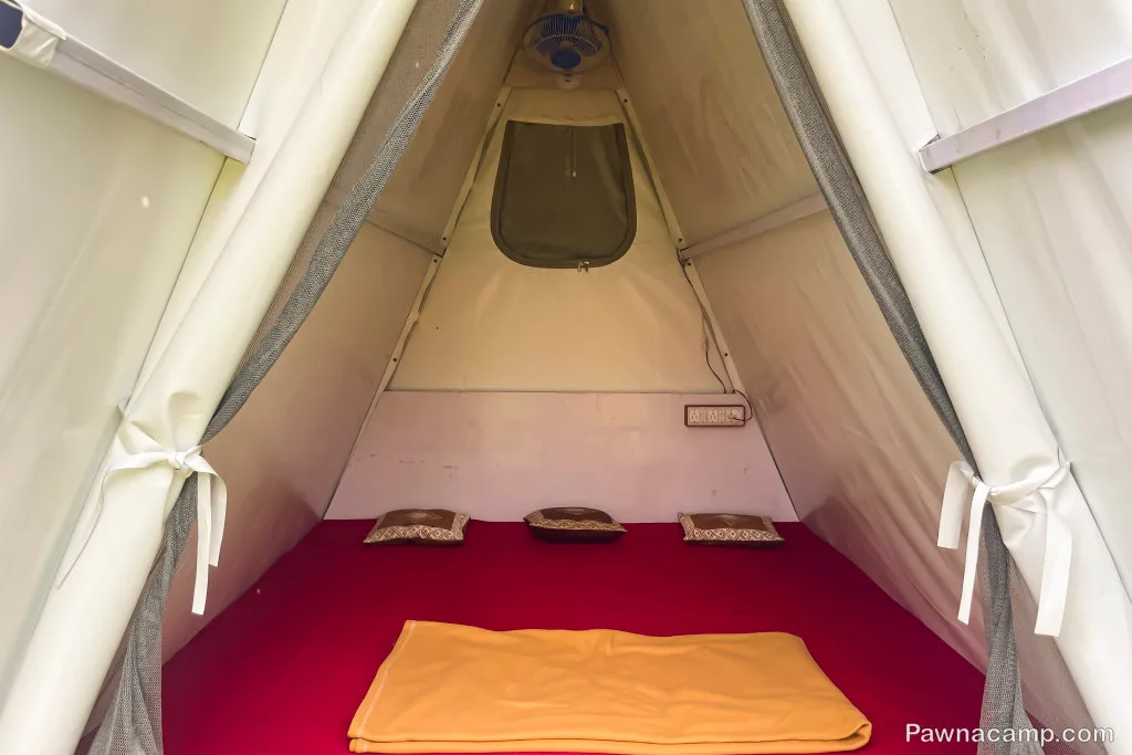 Interior of a cozy tent at Pawna Lake stay, featuring a red mattress, pillows, and a folded blanket inside the triangular structure.