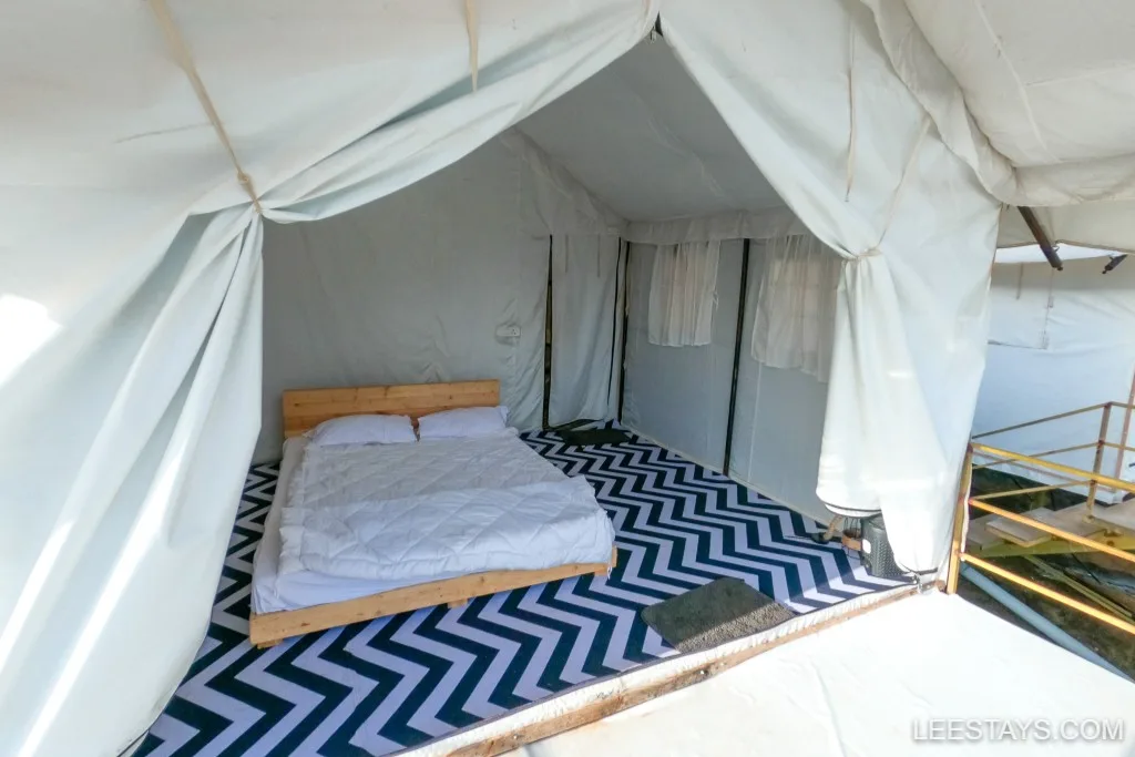 A cozy glamping tent near Pawna Lake with a wooden bed and chevron-patterned flooring, offering a comfortable outdoor accommodation experience.