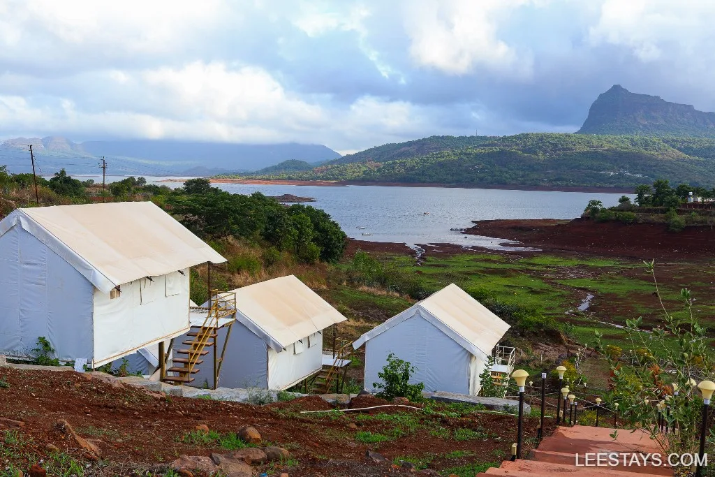 Glamping tents overlooking Pawna Lake, surrounded by lush hills, offering a scenic and peaceful retreat amidst nature.