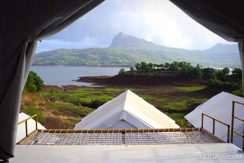 View from a glamping tent at Pawna Lake, featuring lush green hills and a serene water body under a cloudy sky.