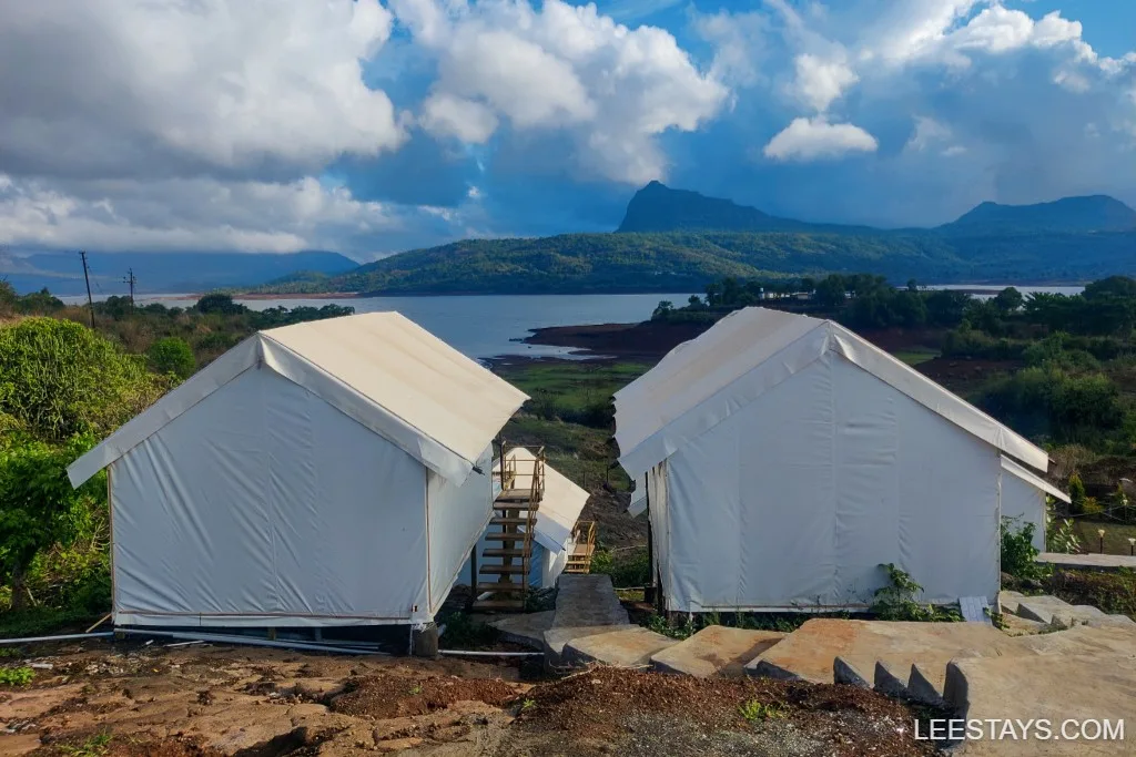 Glamping tents near Pawna Lake with scenic views of the hills and lush landscape, offering a serene outdoor experience under a partly cloudy sky.