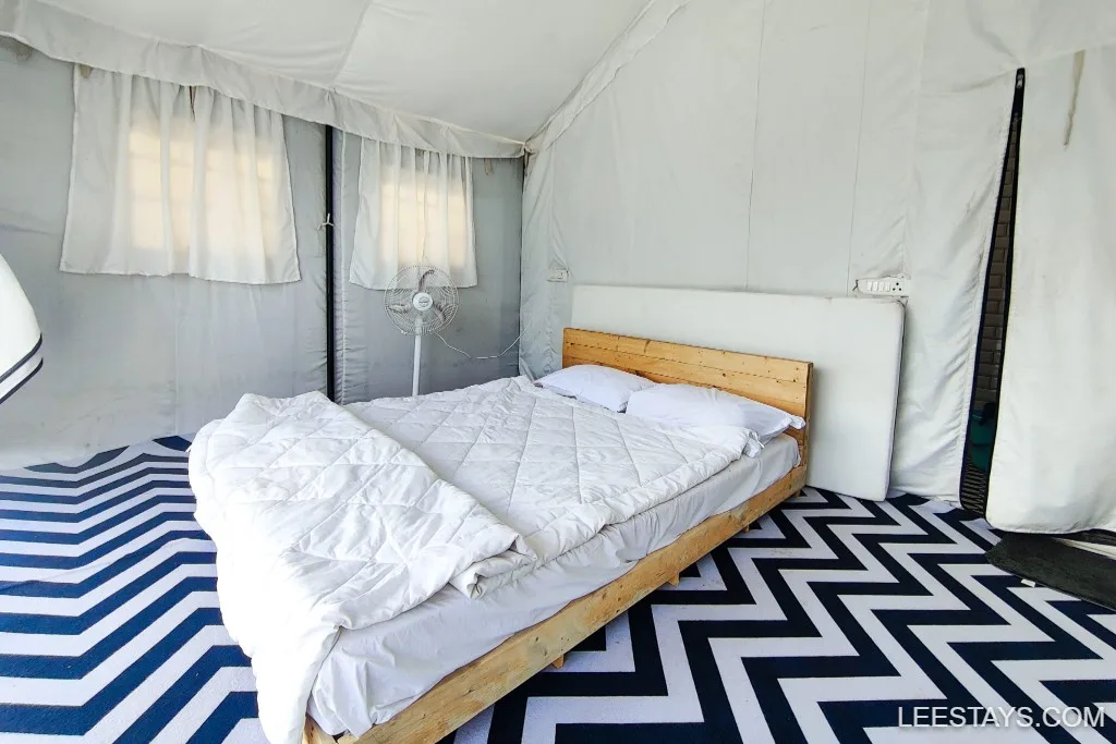 Interior of a luxury glamping tent near Pawna Lake, featuring a wooden bed with white bedding and a zigzag patterned carpet.