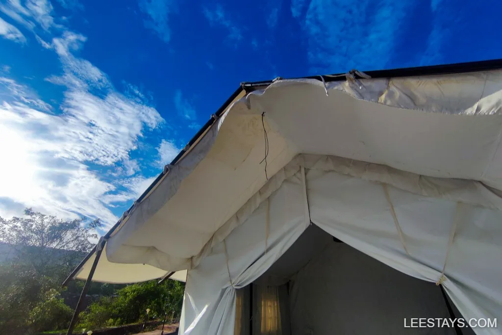 View of a glamping tent at Pawna Lake under a clear blue sky, showcasing modern outdoor accommodation with natural surroundings.
