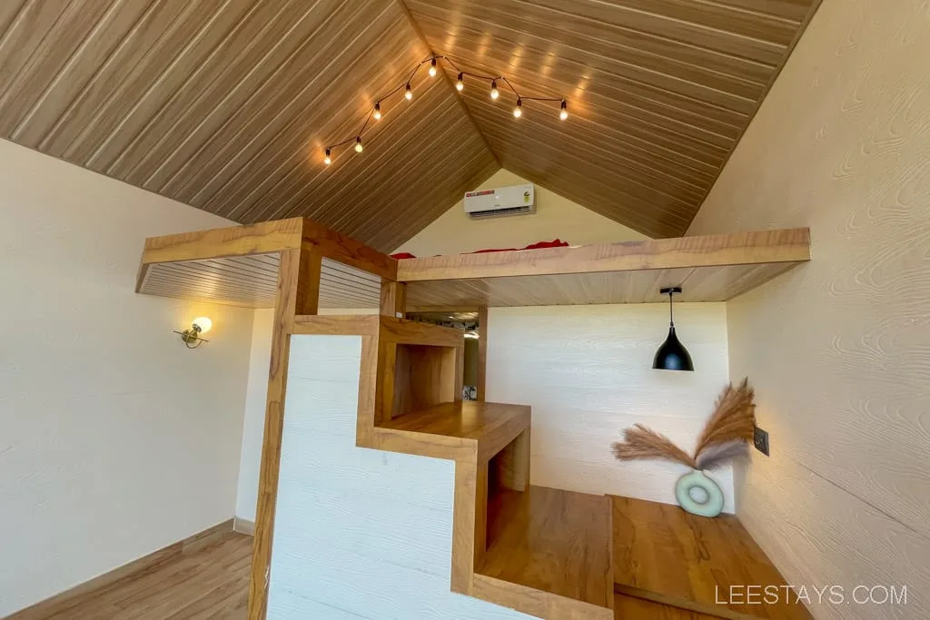 Cozy interior of a wooden cabin with a small loft, located near glass rooms at Pawna Lake, featuring a pendant light and decorative elements.