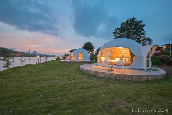 Glamping domes at Domestory Resort by Malvandi Lake during sunset, featuring illuminated interiors and surrounding greenery.