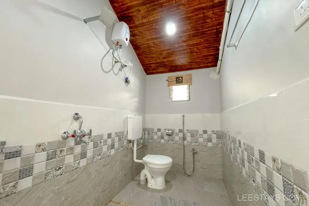 Bathroom in a riverside cottage near Pawna Lake, featuring a toilet, shower area, and tiled walls with a wooden ceiling.