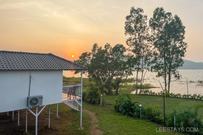 A picturesque view of a Pawna lakeview cottage, ideal for couple friendly stays, with a serene lake, vibrant sunset, and surrounding trees.
