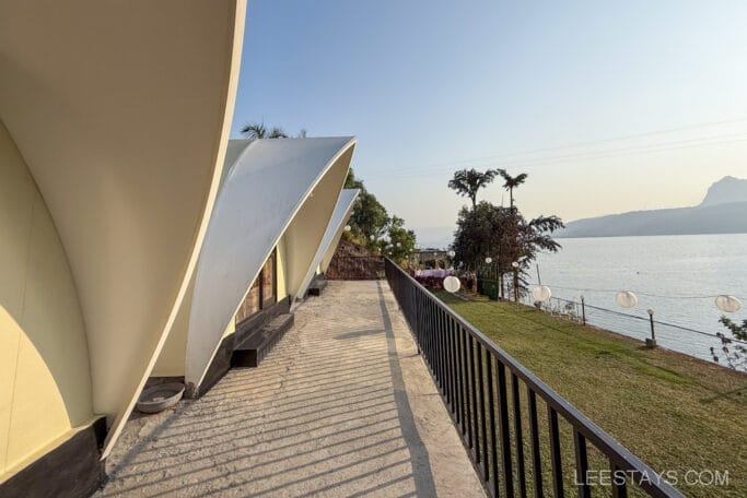 A glamping site near Pawna Lake featuring modern tented structures with white arches, overlooking a serene lake and surrounded by greenery and lanterns.