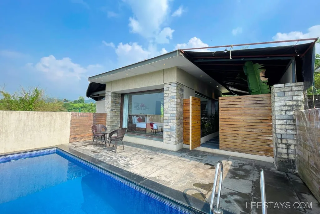 Resort near Pawna Lake featuring a modern building with a private swimming pool, outdoor seating, and lush greenery under a bright blue sky.